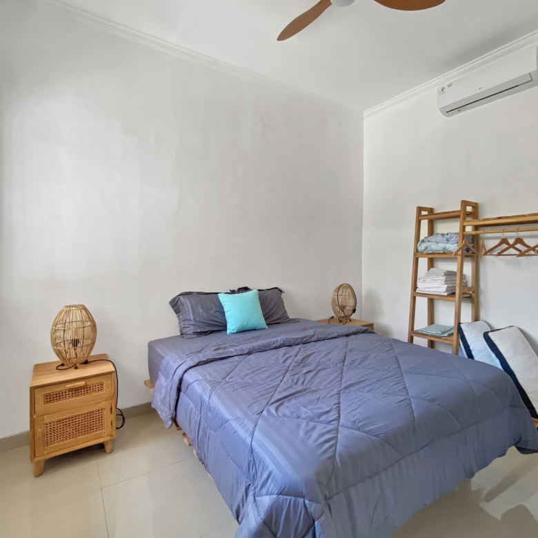 Twin bedroom with two single beds in blue comforters, a wooden nightstand with a wicker lamp, and a wall-mounted clothes rack.