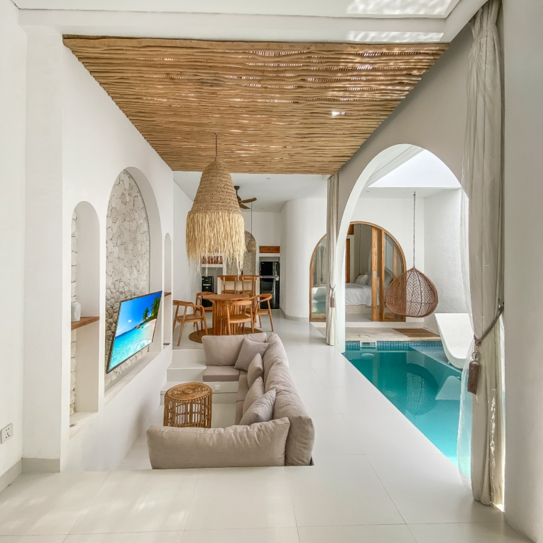 Open living area with white walls, arched doorways, a large woven pendant light, wooden dining set, and a view of the indoor pool.