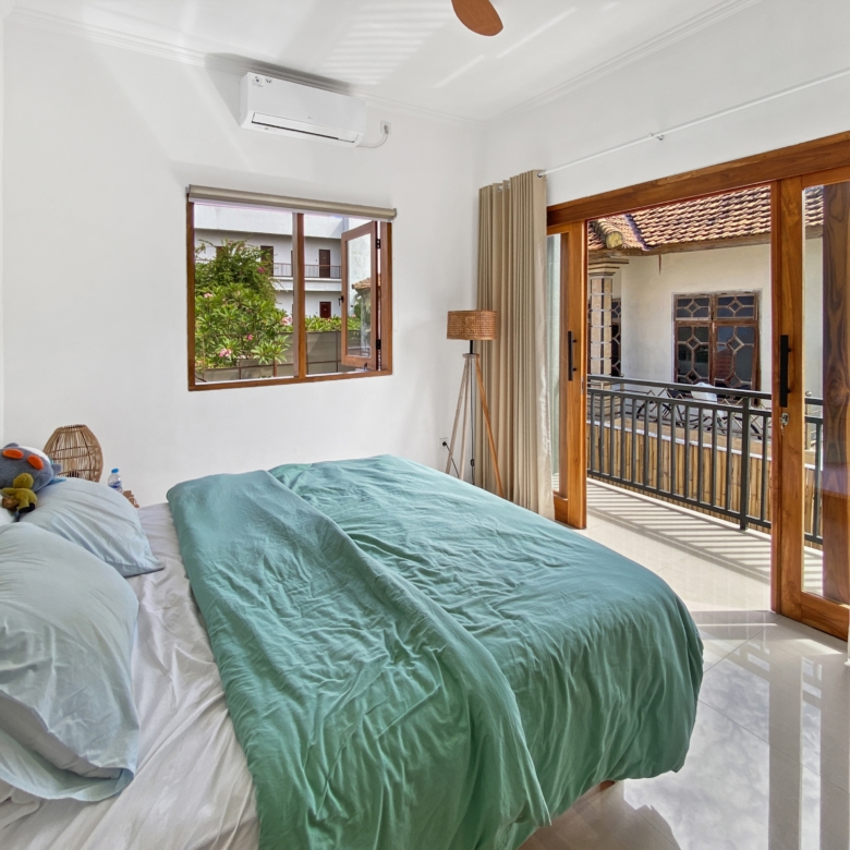 Bright hotel-style bedroom with two neatly made beds, teal blankets, and a small stuffed toy on white sheets.