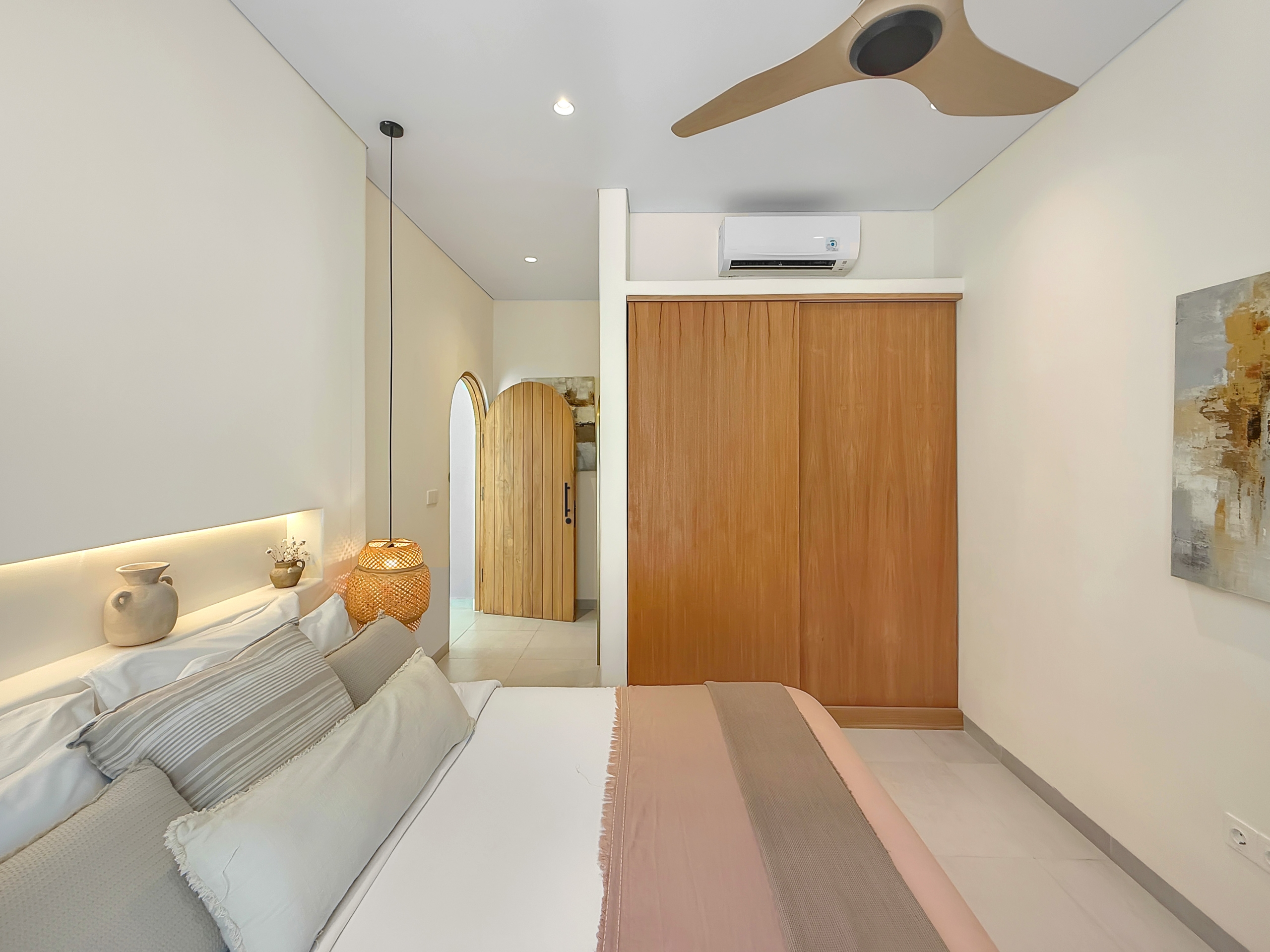 0989930e0b3ba3ae7bcc8078394736d588aa77c6 Two neatly made twin beds with beige bedding and decorative cushions in a modern bedroom, next to a wooden wardrobe and warm lighting.