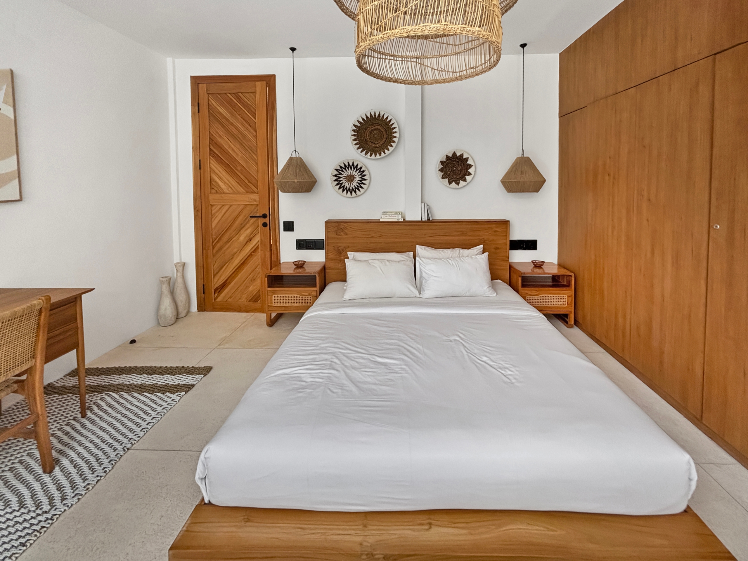 0b8efa9556f42ba4aa24fb7247a1fcb14755021e Wooden-framed bed with white bedding, two nightstands, and woven pendant lights in a bright white room with wooden accents.