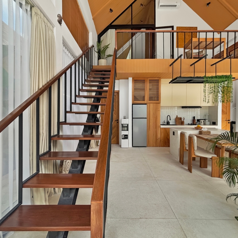 Open-concept interior with a wooden staircase along a glass wall, black railings, and a kitchen below on the right.