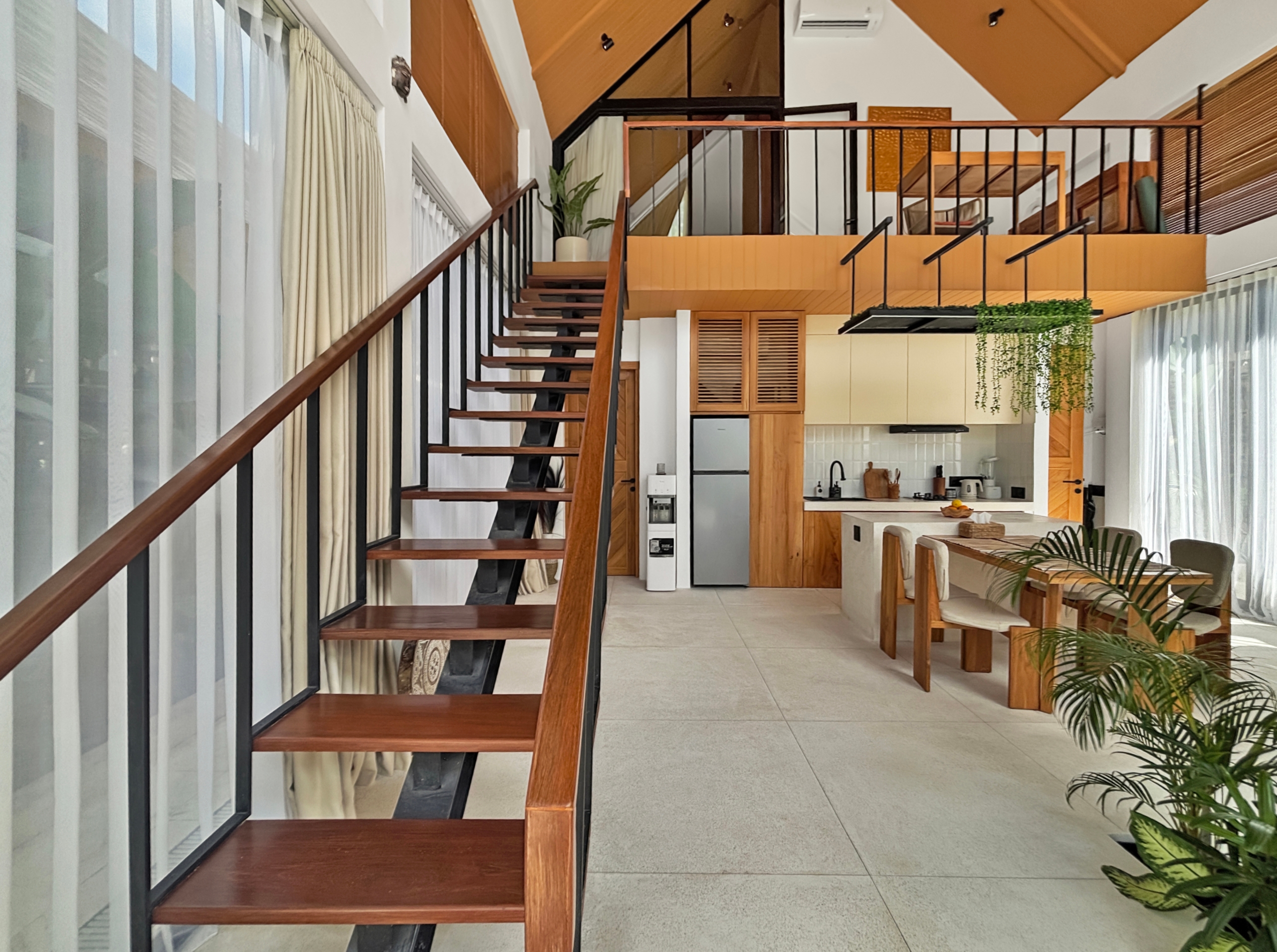 0de7e503ef9736198e3b4d727c26ab80e750cf1d Open-concept interior with a wooden staircase along a glass wall, black railings, and a kitchen below on the right.