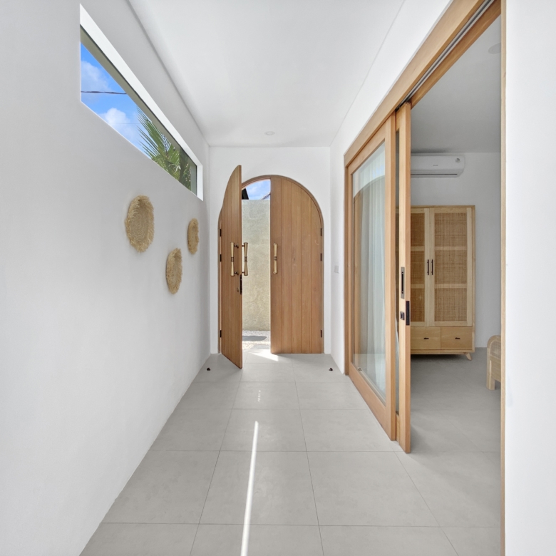 Bright indoor hallway with white walls, wooden-framed glass doors, and an arched doorway at the end, plus wall decor on the left.