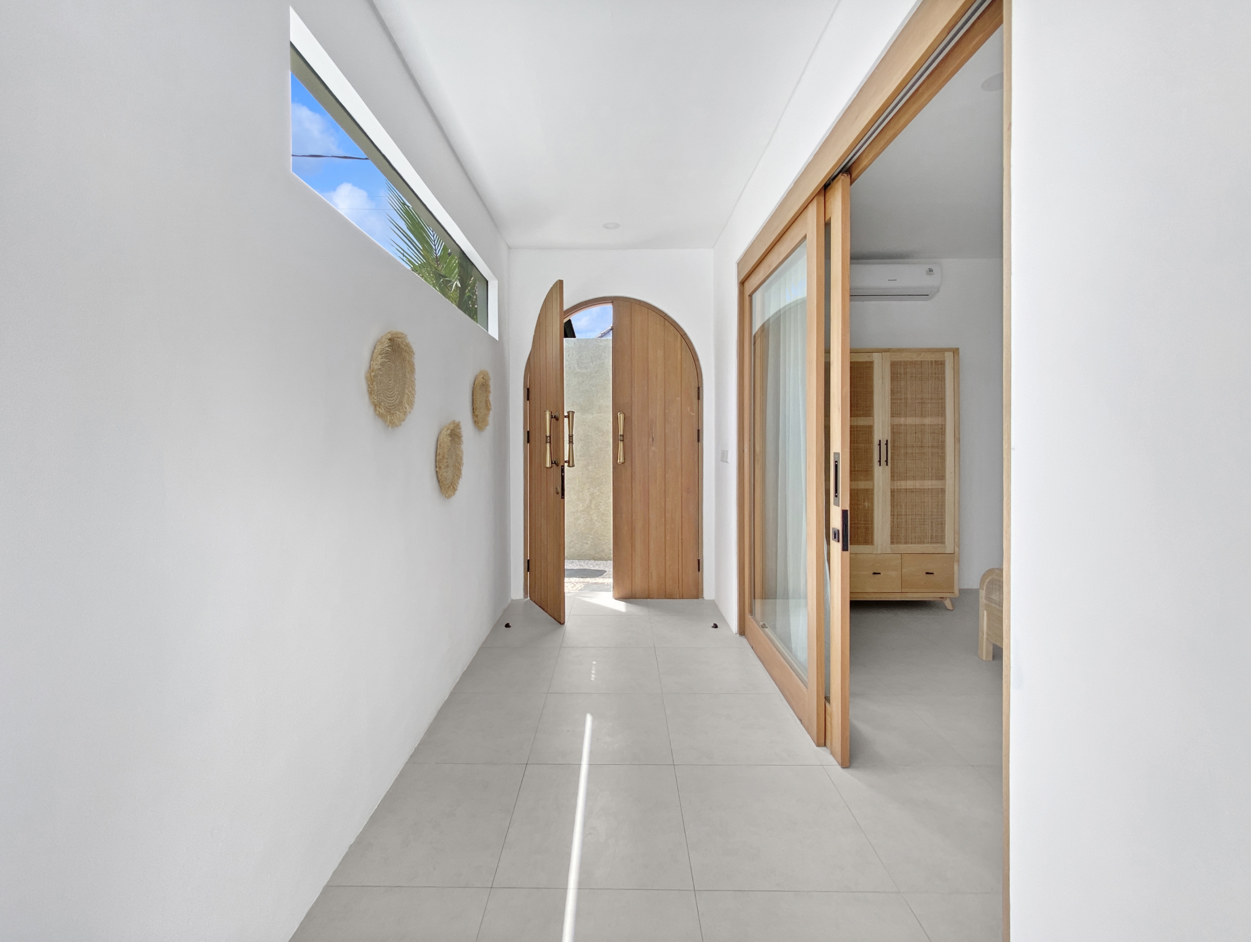 1430e922576a146fa02150b7e3b67b282fbedda8_2299-68d5cfb037739 Bright indoor hallway with white walls, wooden-framed glass doors, and an arched doorway at the end, plus wall decor on the left.