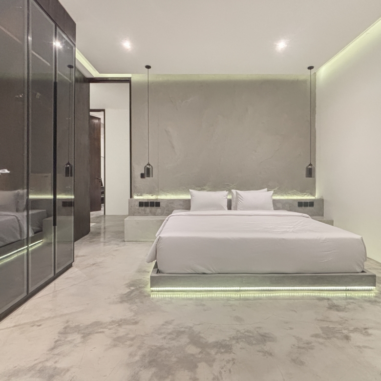 Modern hotel bedroom with a low platform bed, white bedding, and glass-front wardrobes along the left wall.