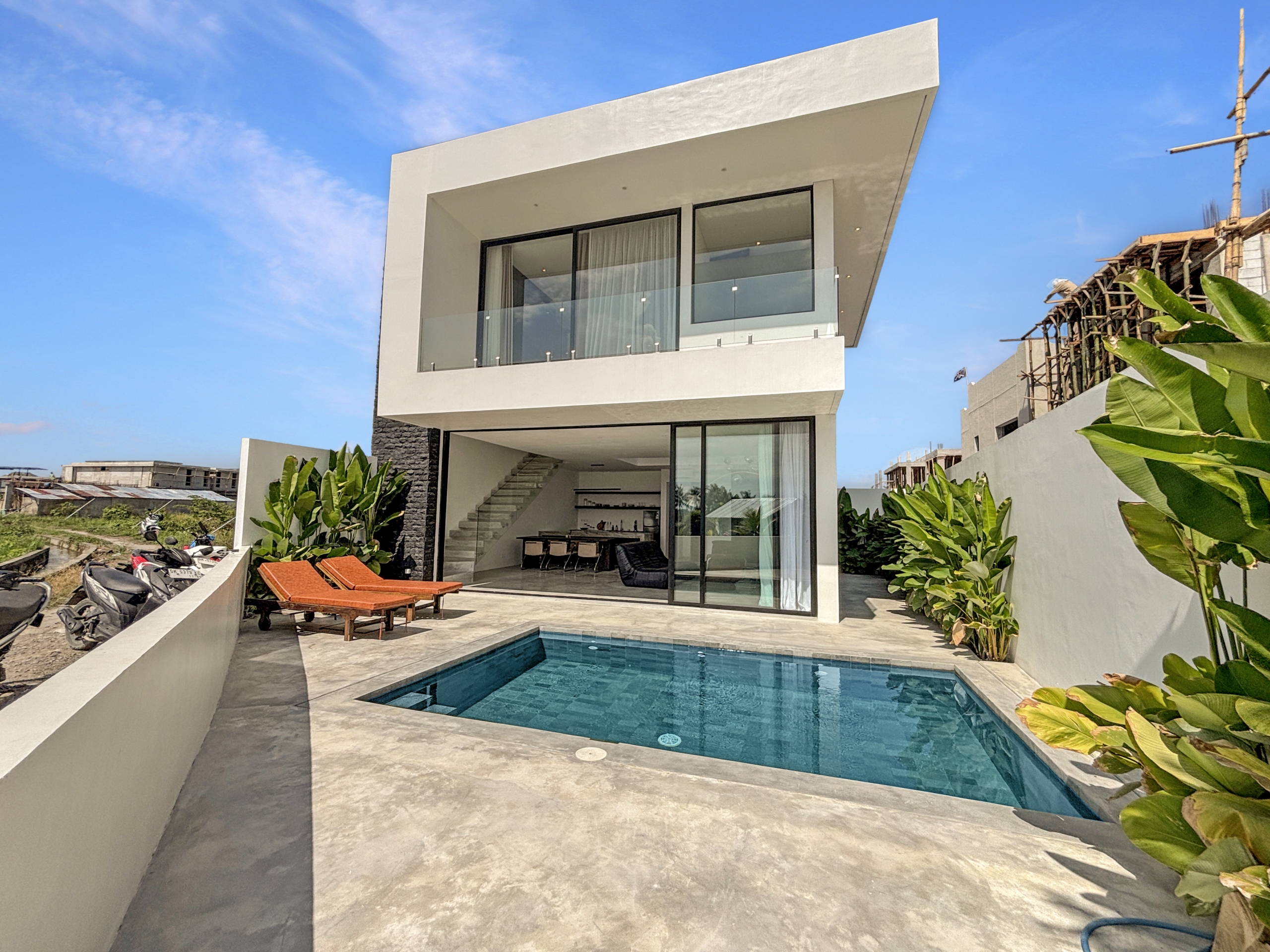 3dccdb18c27f12ce8cf9ea9b76f05696bb4b5304_6786-6a1d7bace102d Modern white multi‑level house with large glass walls and a rectangular swimming pool in the foreground under a clear blue sky.