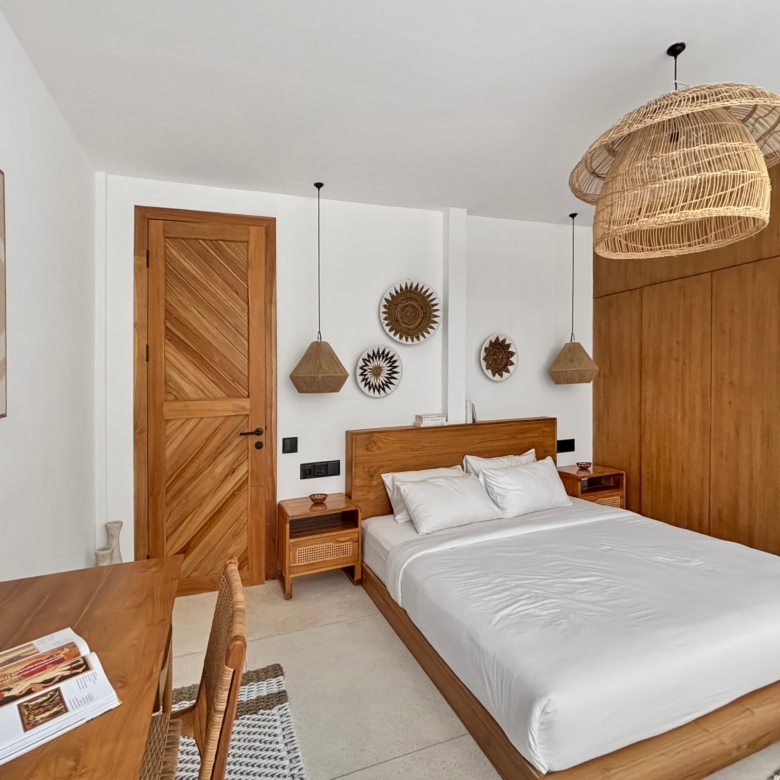 Hotel bedroom with two single beds, wooden headboards, nightstands, and woven rattan pendant lights against white walls and wood paneling.