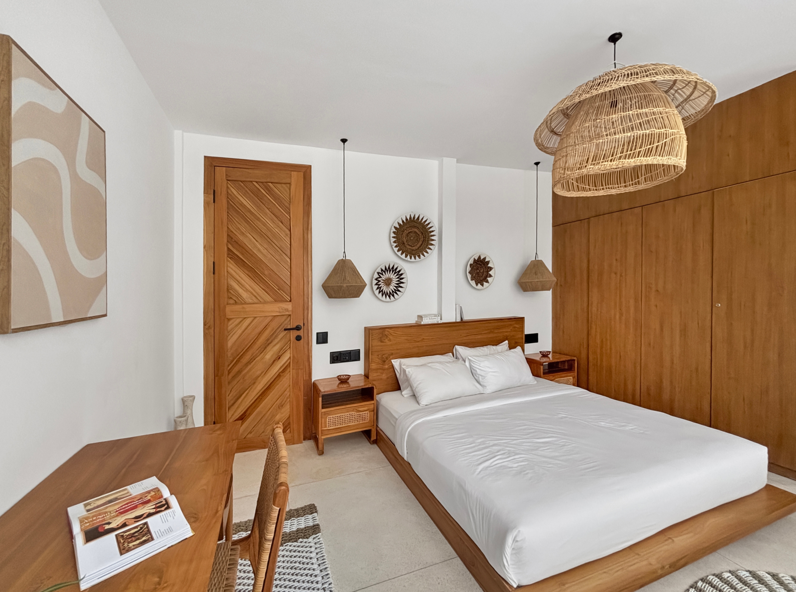 3fb708b81b1490d7cac9dfcd494c3703fab923d7 Hotel bedroom with two single beds, wooden headboards, nightstands, and woven rattan pendant lights against white walls and wood paneling.