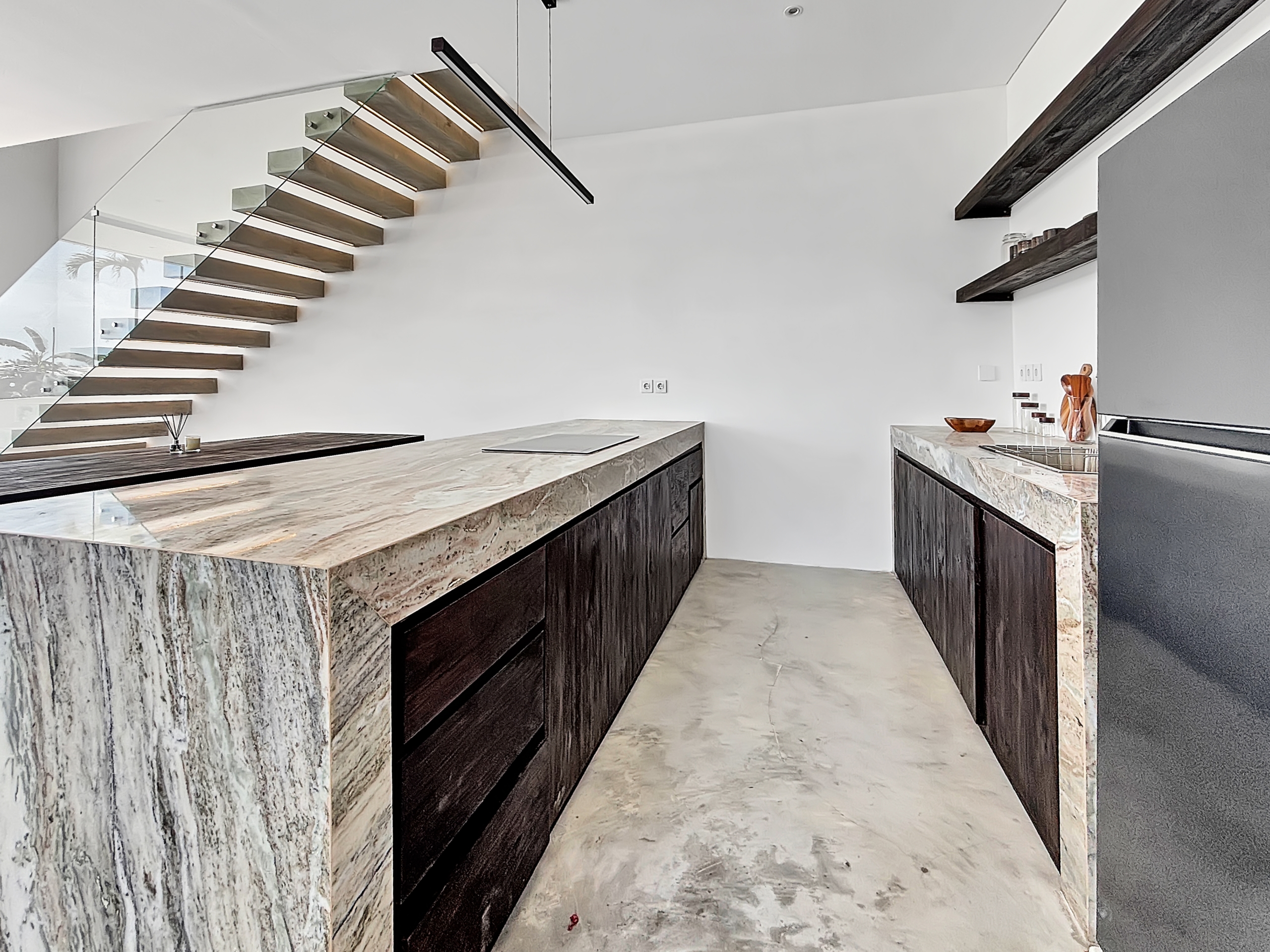 452404fb0437914fdb9a5eb9ea13791584d8973a_6801-6a1d7bae5ad8b Modern kitchen with marble island, dark wood cabinets, and a glass-railed floating staircase along the left wall.
