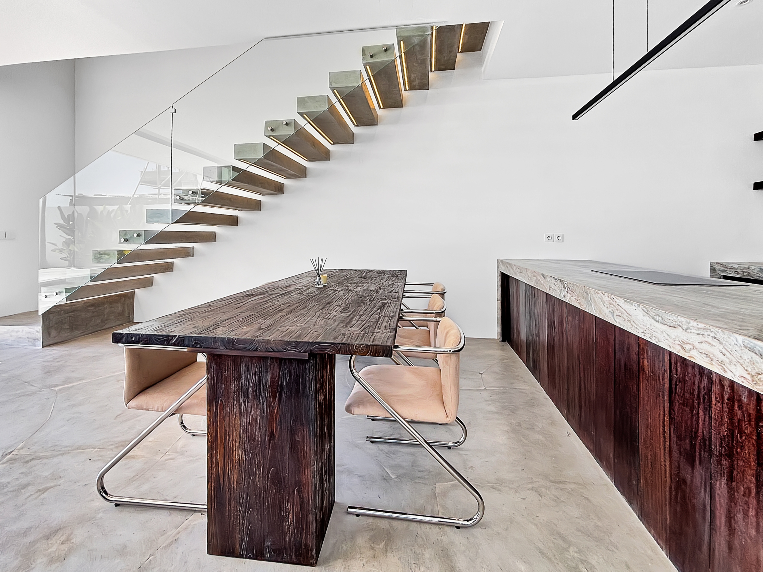 4687e4d60883567f151f526886784441793be40f_6798-6a1d7bae8d06e Modern interior with a diagonal floating wooden staircase and glass railing beside a large dark wood dining table and tan chairs; bright and minimal.