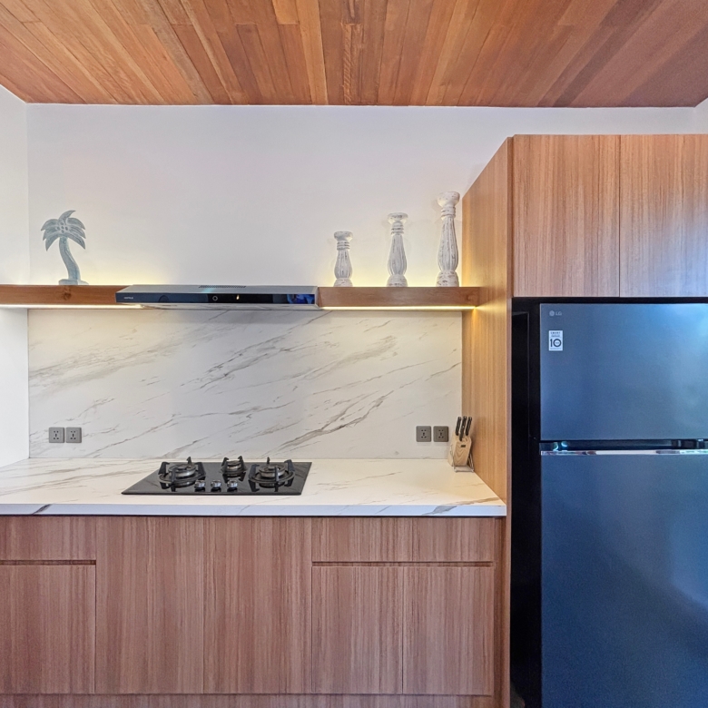 Modern kitchen with marble countertop, gas stove, and wooden cabinets; a shelf displays a palm statue and three white decorative pillars.