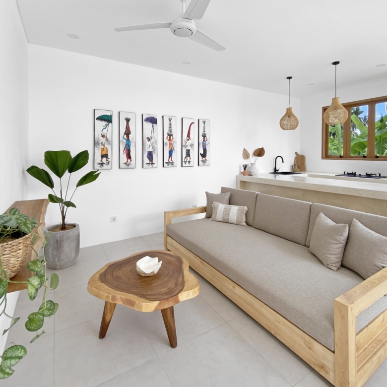 Bright, minimalist living room with a beige sofa, live-edge wooden coffee tables, and potted plants; seven framed art pieces line a white wall.