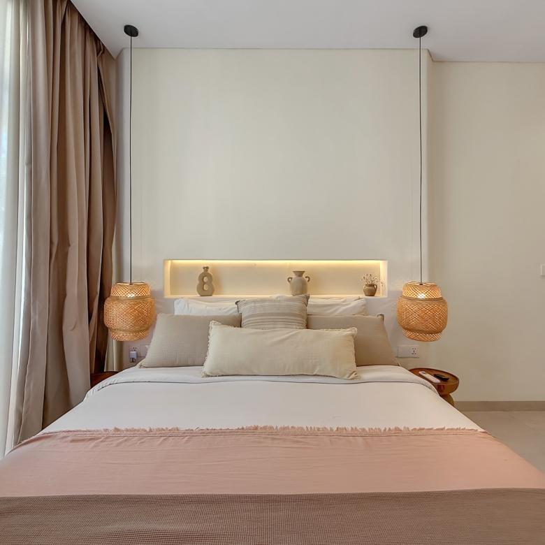 Cozy hotel bedroom with a large bed, beige linens, woven pendant lamps, and pale curtains on the left side.