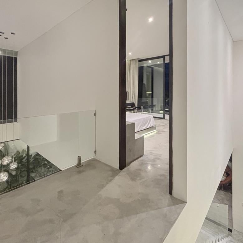 Modern interior with glass railing and hanging spherical pendant lights, leading to a doorway showing a bedroom beyond.