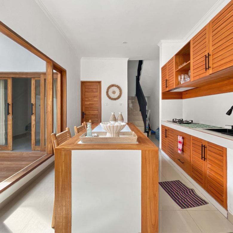 Bright kitchen and dining area with warm wooden cabinets, a central wooden dining table, and glass sliding doors.