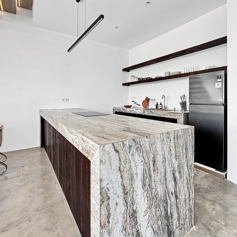Modern kitchen featuring a marble island, dark wood accents, open shelves with glassware, and a stainless steel refrigerator.