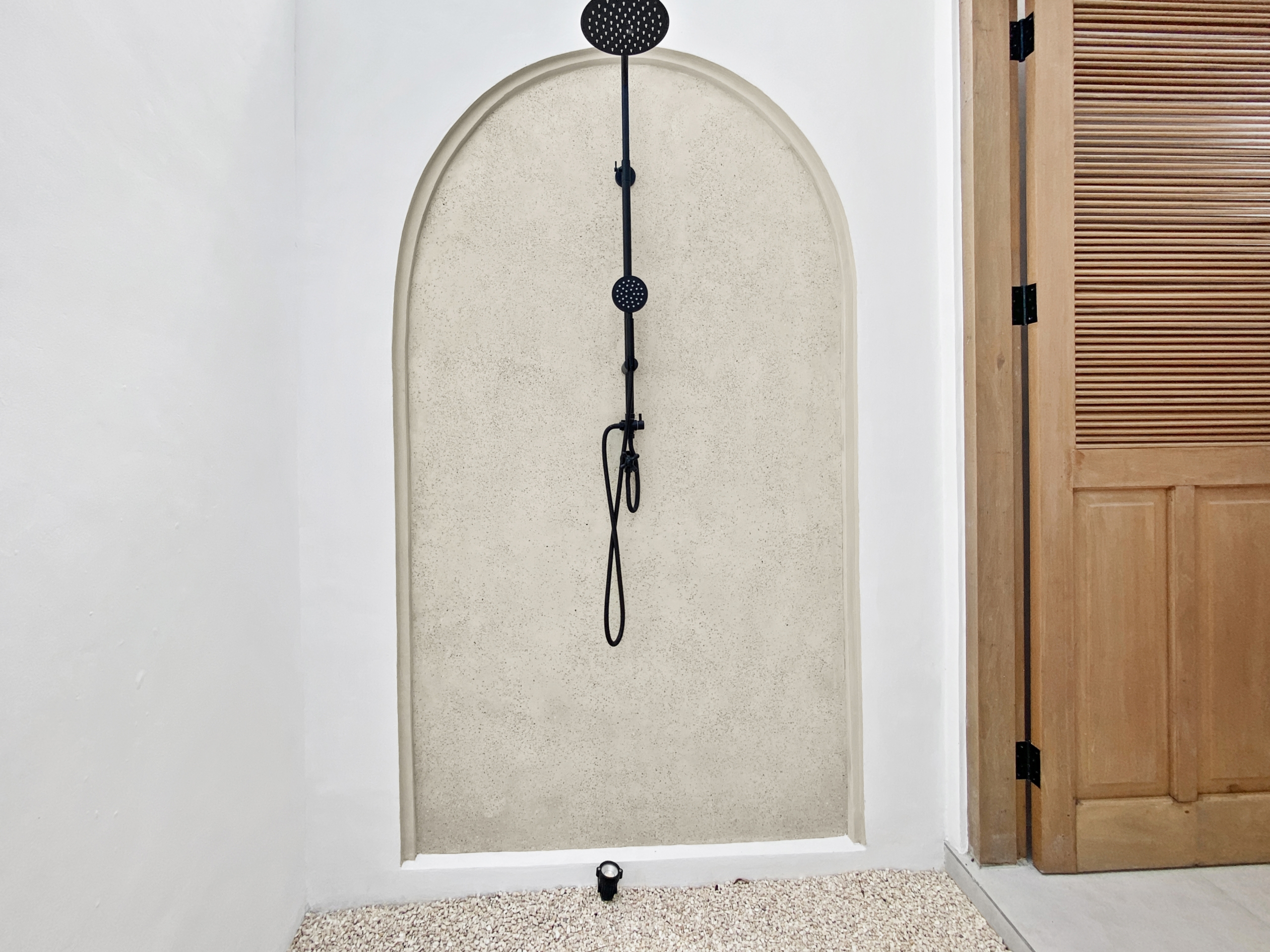63c360da3c50deda70bb03414e42cd187f4ea4b1_2312-68d5cfb1e7a01 Narrow shower alcove with a vertical shower rail and two round shower heads mounted on a white wall, wood door to the right.