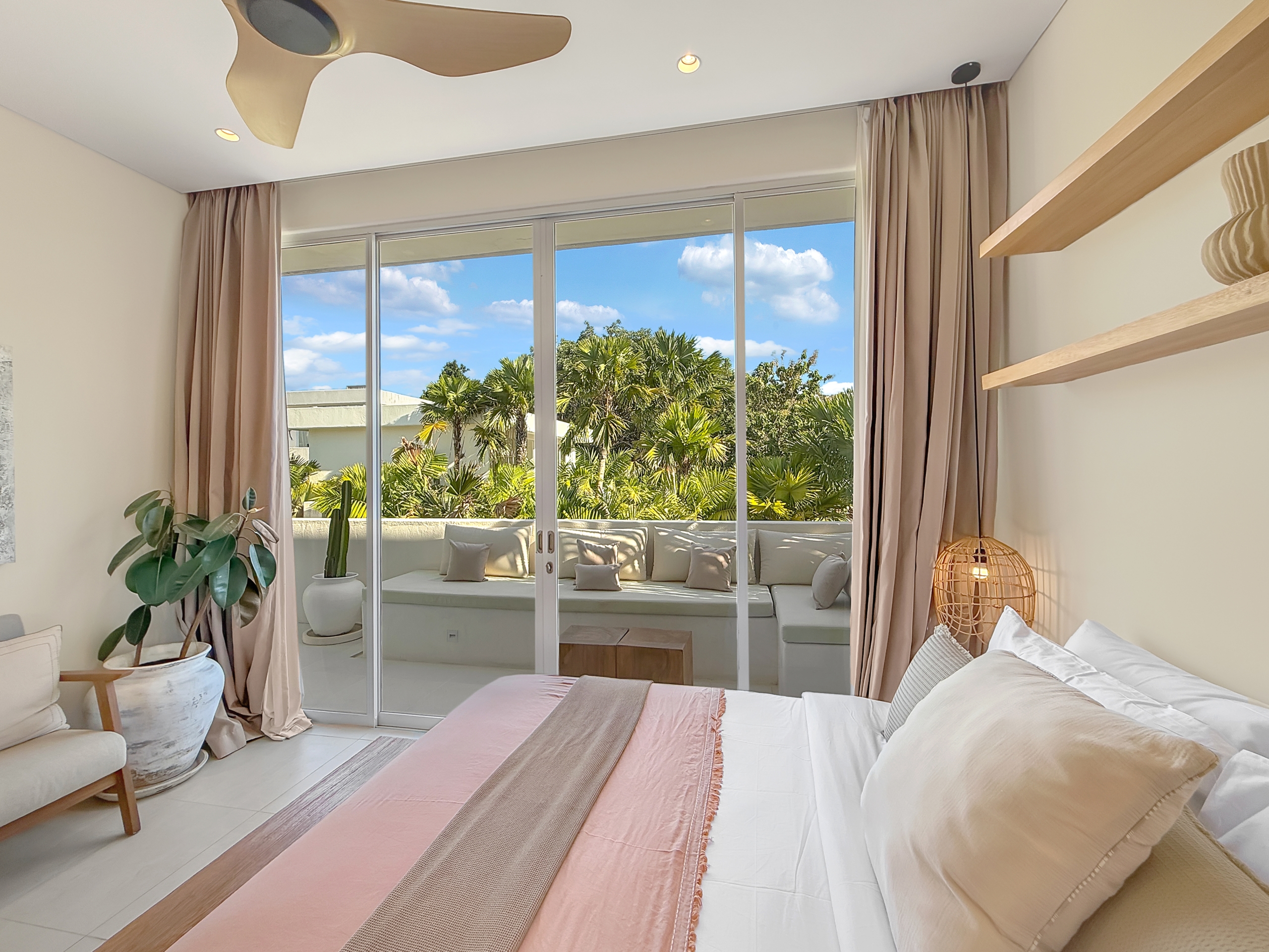 682349c03721477a5fd1a851e19f0e5ea02cdc47 Bright bedroom with sliding glass doors opening to a sunny balcony, beige curtains, and several potted plants inside.