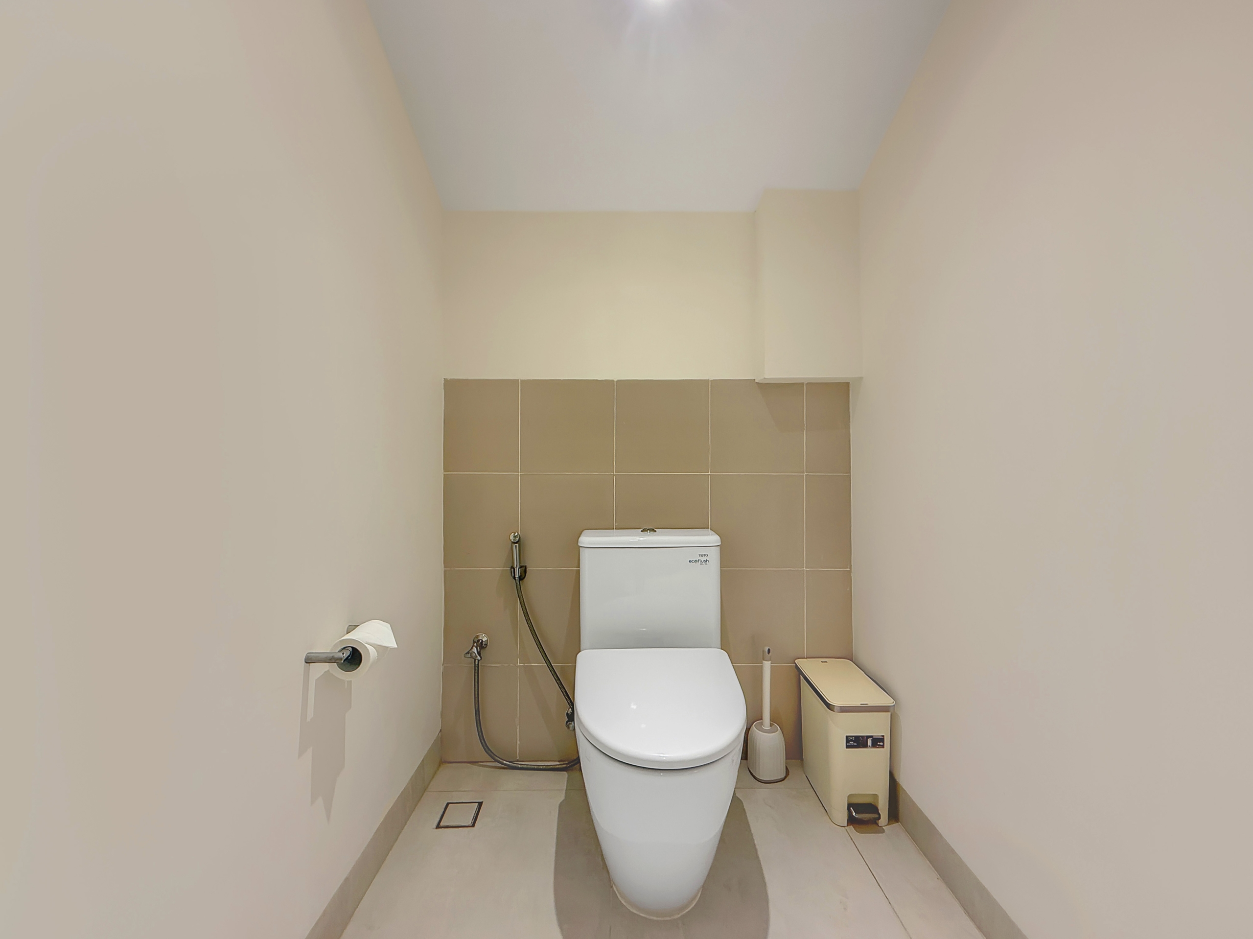6a2b43832f84290b5679ece274c3f6c3b18be25b Narrow bathroom with beige walls and brown-tile backsplash, featuring a white toilet and a bidet spray hose to its left.