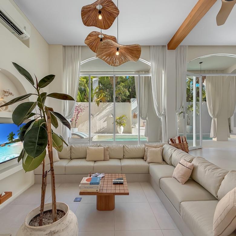 Bright living room with white sectional sofa, large glass doors to a sunny tropical courtyard and potted plant nearby.