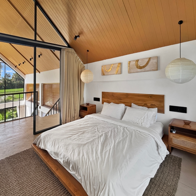 Bright bedroom with twin beds on a wooden platform, a warm wood ceiling, paper pendant lights, and large glass windows opening to greenery.