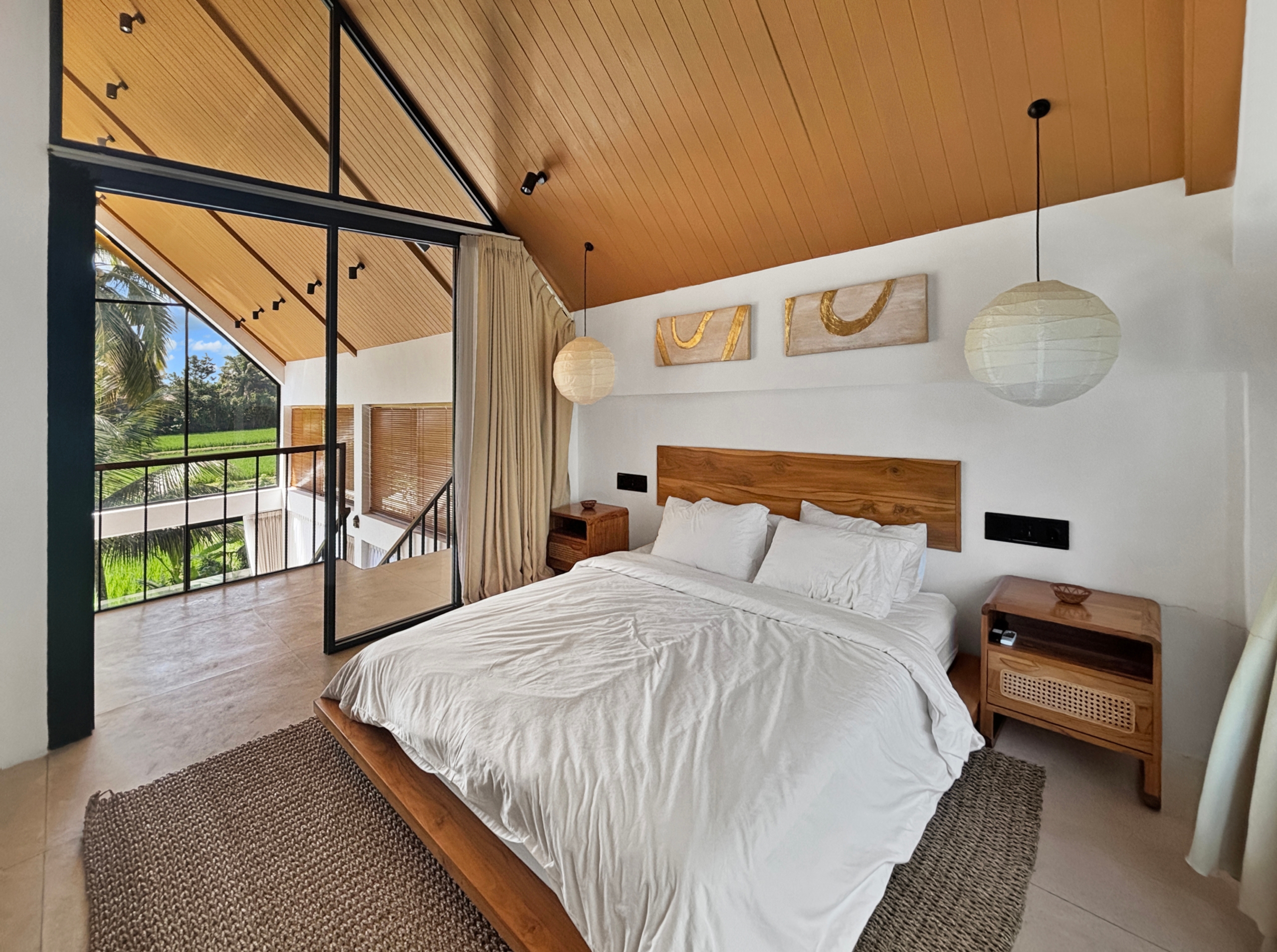 71b5083c29df43a8bef35a079d2b2c527c1603df Bright bedroom with twin beds on a wooden platform, a warm wood ceiling, paper pendant lights, and large glass windows opening to greenery.