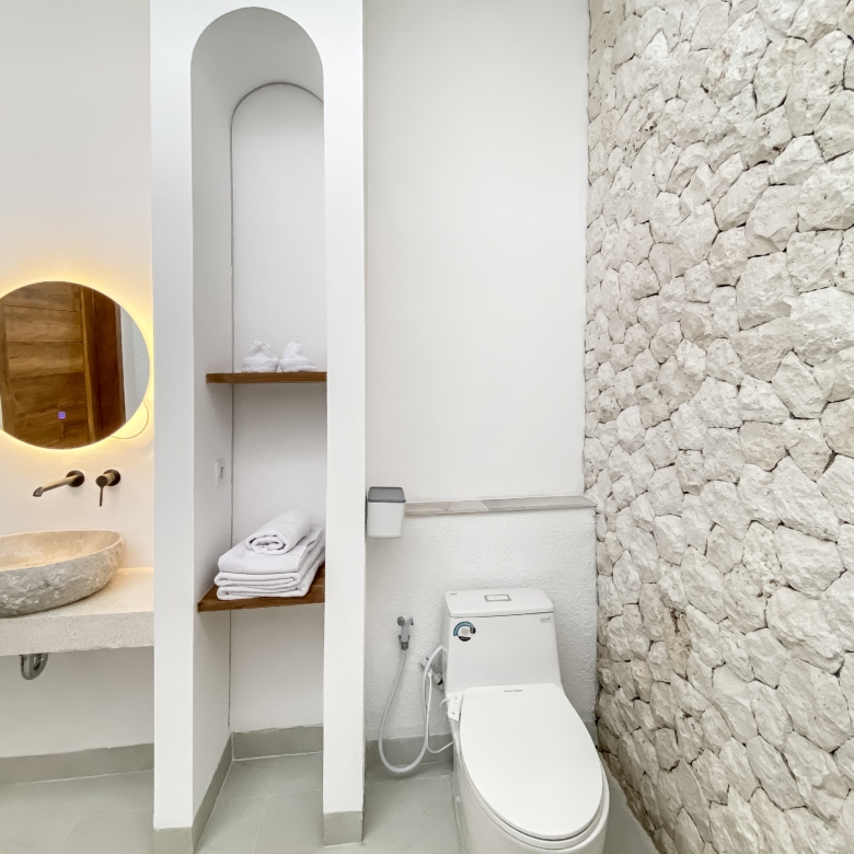 Modern bathroom interior featuring a round backlit mirror above a stone sink, white shelves, and a stacked stone wall on the right.] ,