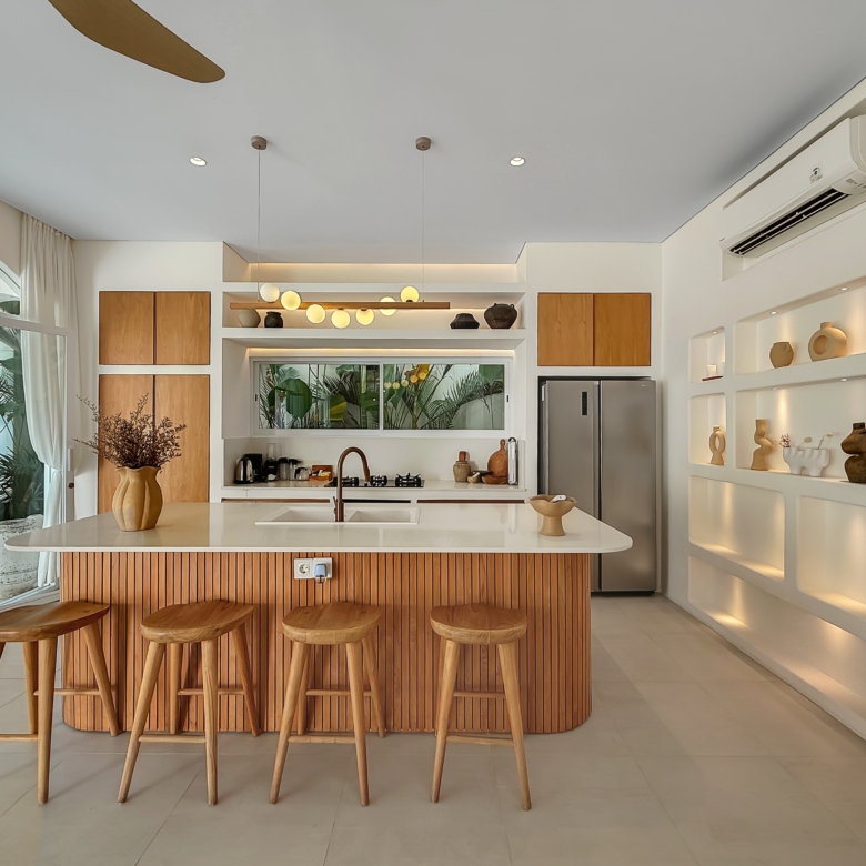 Open-plan kitchen with a large wooden island and four wooden bar stools, white cabinets, and built-in shelves displaying pottery items.