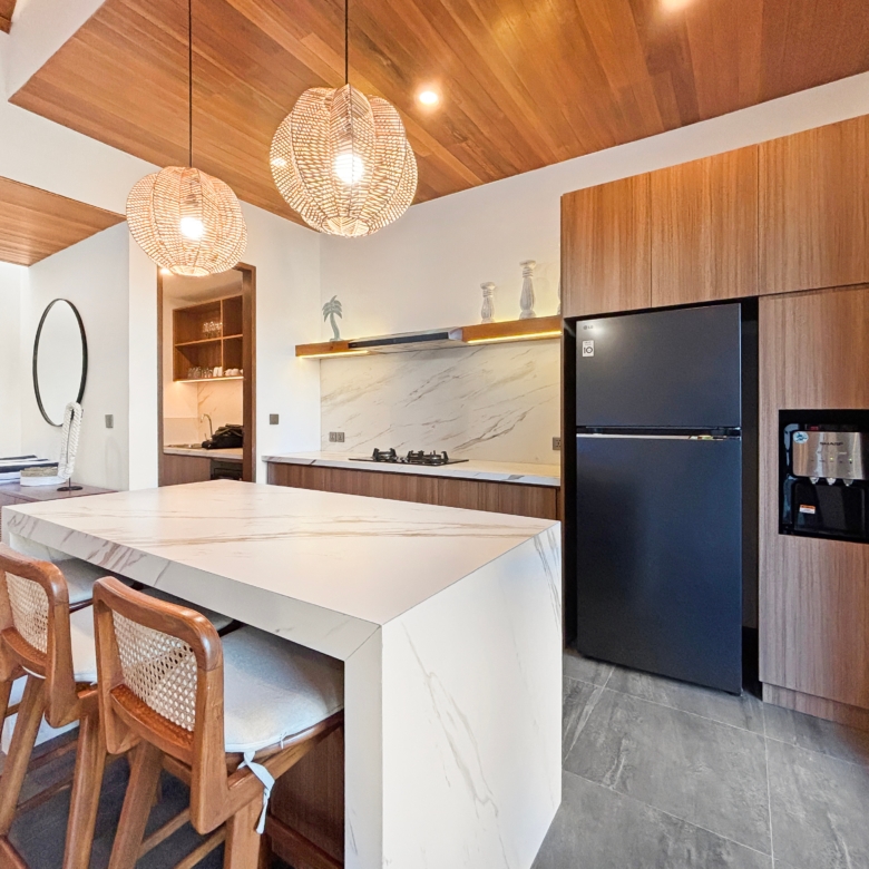 Open-plan kitchen with marble island, wooden bar stools, and warm woven pendant lights above the counter.