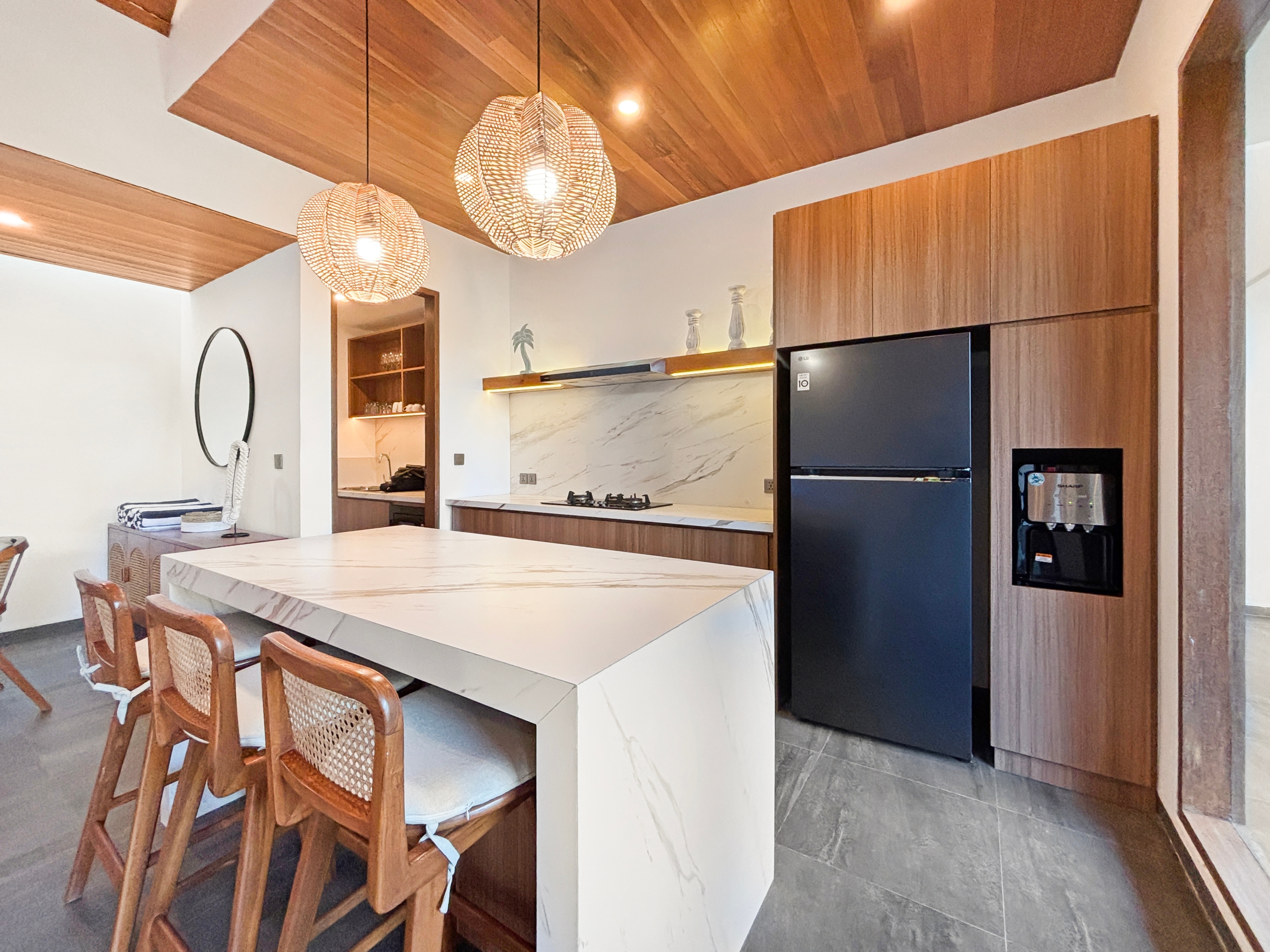 83aed40491b86f37dcacb1381b8d73aee9564280 Open-plan kitchen with marble island, wooden bar stools, and warm woven pendant lights above the counter.