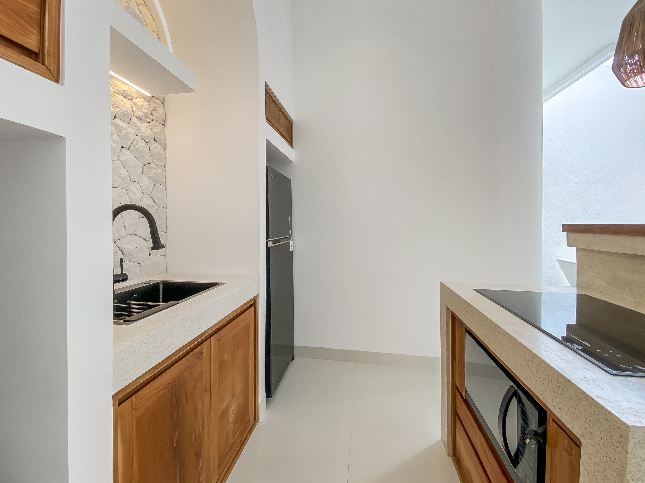 841f721db6bbec60f1ad1553775234a6ac641b83 Modern U-shaped kitchen with white walls, light countertops, wooden lower cabinets, and a stone-tile backsplash around the sink area; black faucet over a double sink.
