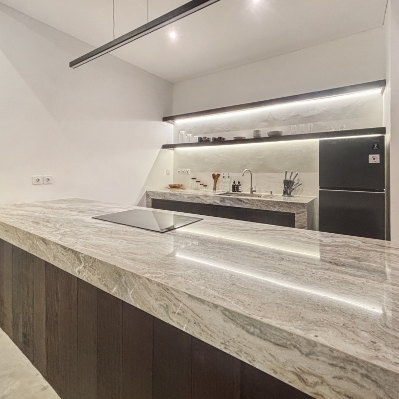 Modern kitchen with marble countertops, open shelves holding dishes, and a stainless steel oven against white walls.