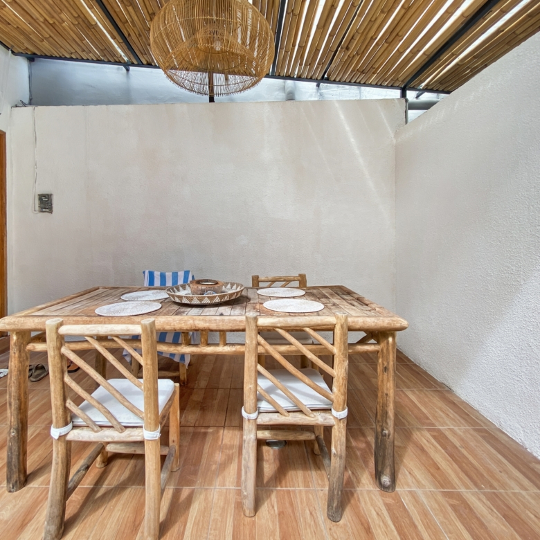 Outdoor dining area with a rustic wooden table and matching chairs under a bamboo ceiling and wicker chandelier, on a tiled veranda.