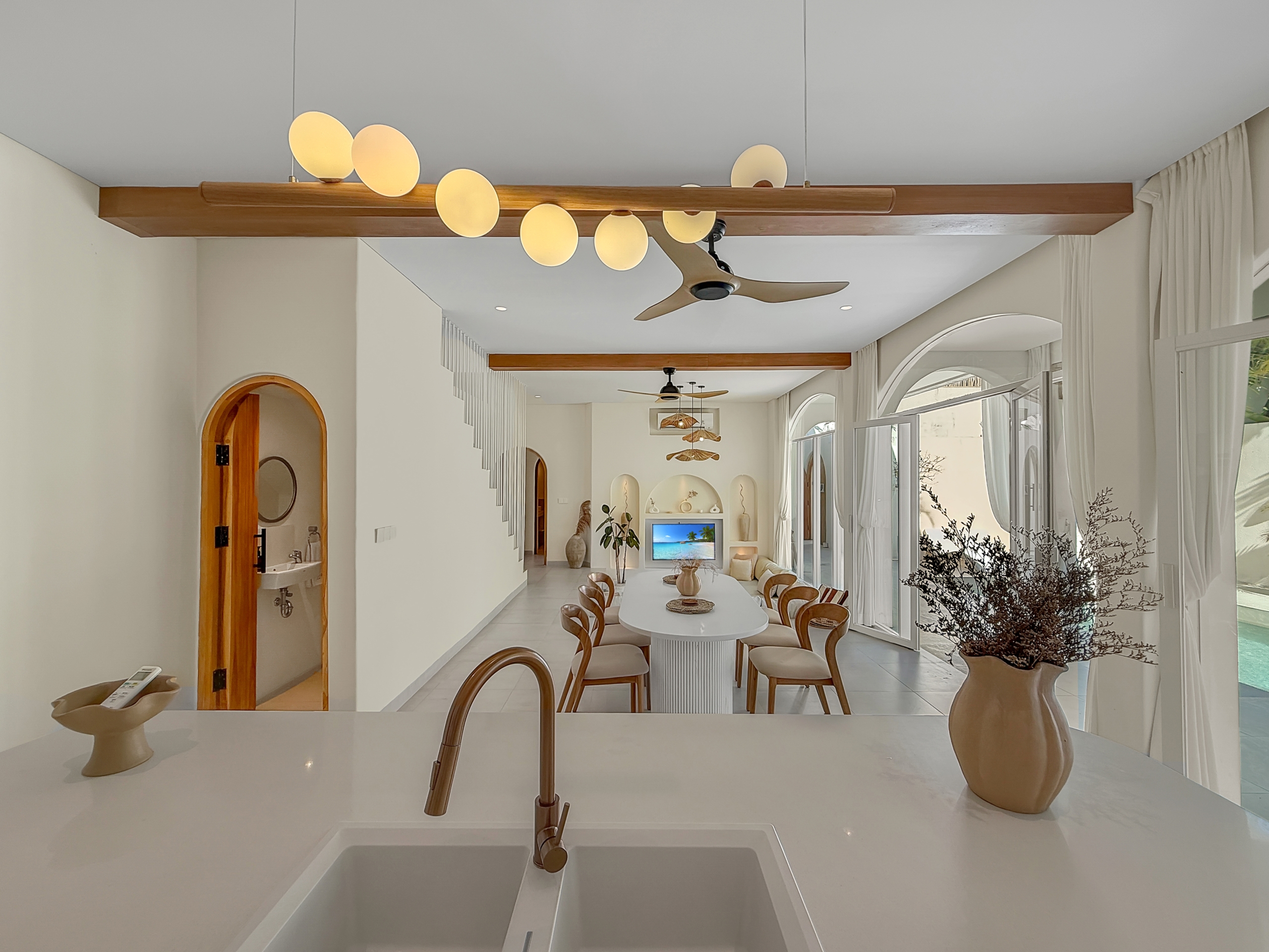 8d68364b44b0e07fea6a7195bd197940076f8343 Open-plan kitchen and dining area with a white island, oval dining table, and wooden chairs under wooden ceiling beams and a ceiling fan.