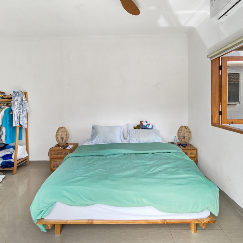 Bedroom with a single bed in mint green bedding, a clothes rack on the left, and an open window on the right.