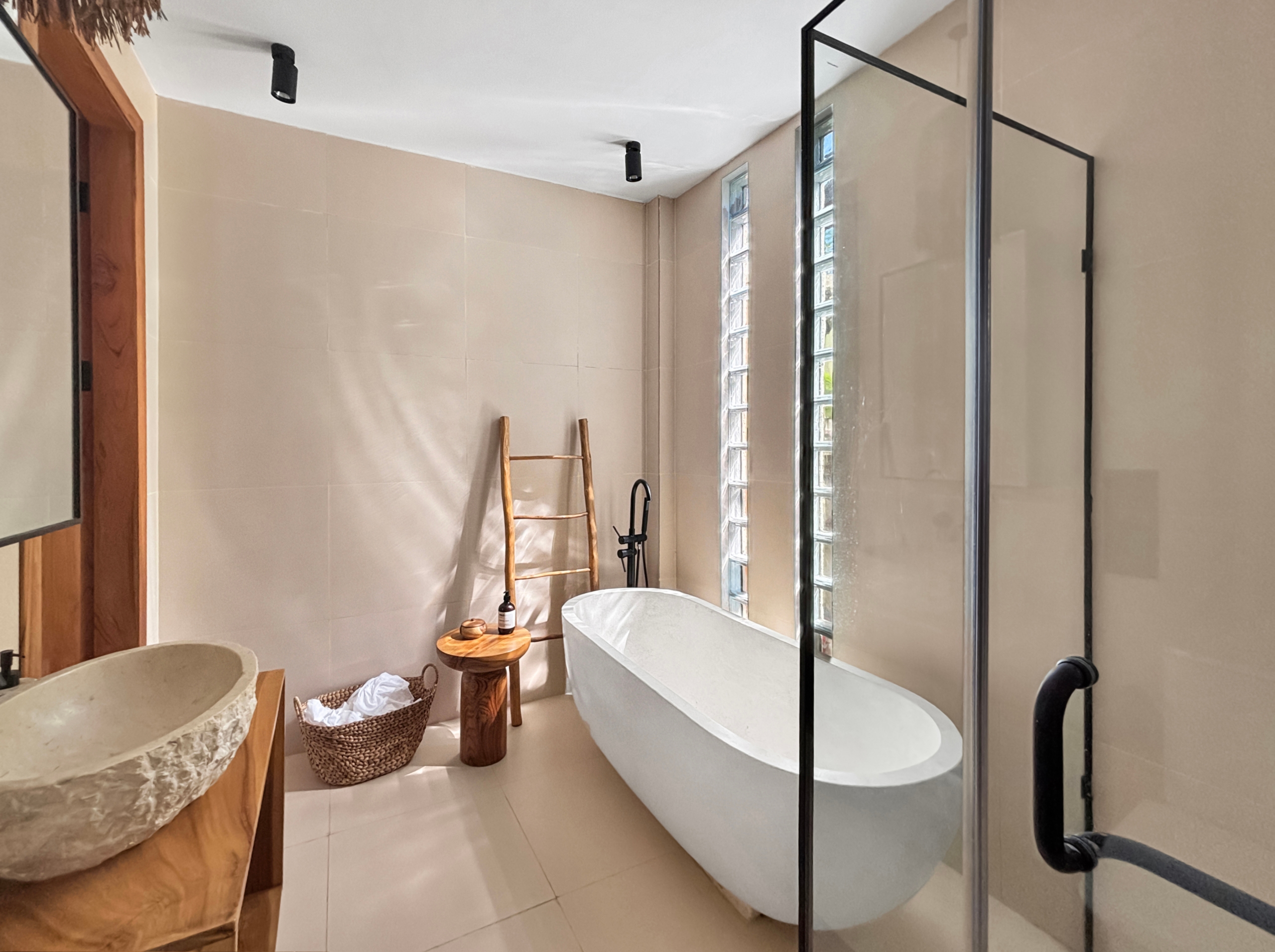 9ec32a46f3217dab5dbb40faaac079421a58d46e Spa-inspired bathroom with a white freestanding tub next to a glass-block window and a glass shower enclosure framed in black metal.