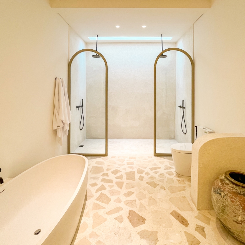 Spa-like bathroom with three arched-brass framed shower enclosures, a freestanding tub on the left, and terrazzo floors intact.