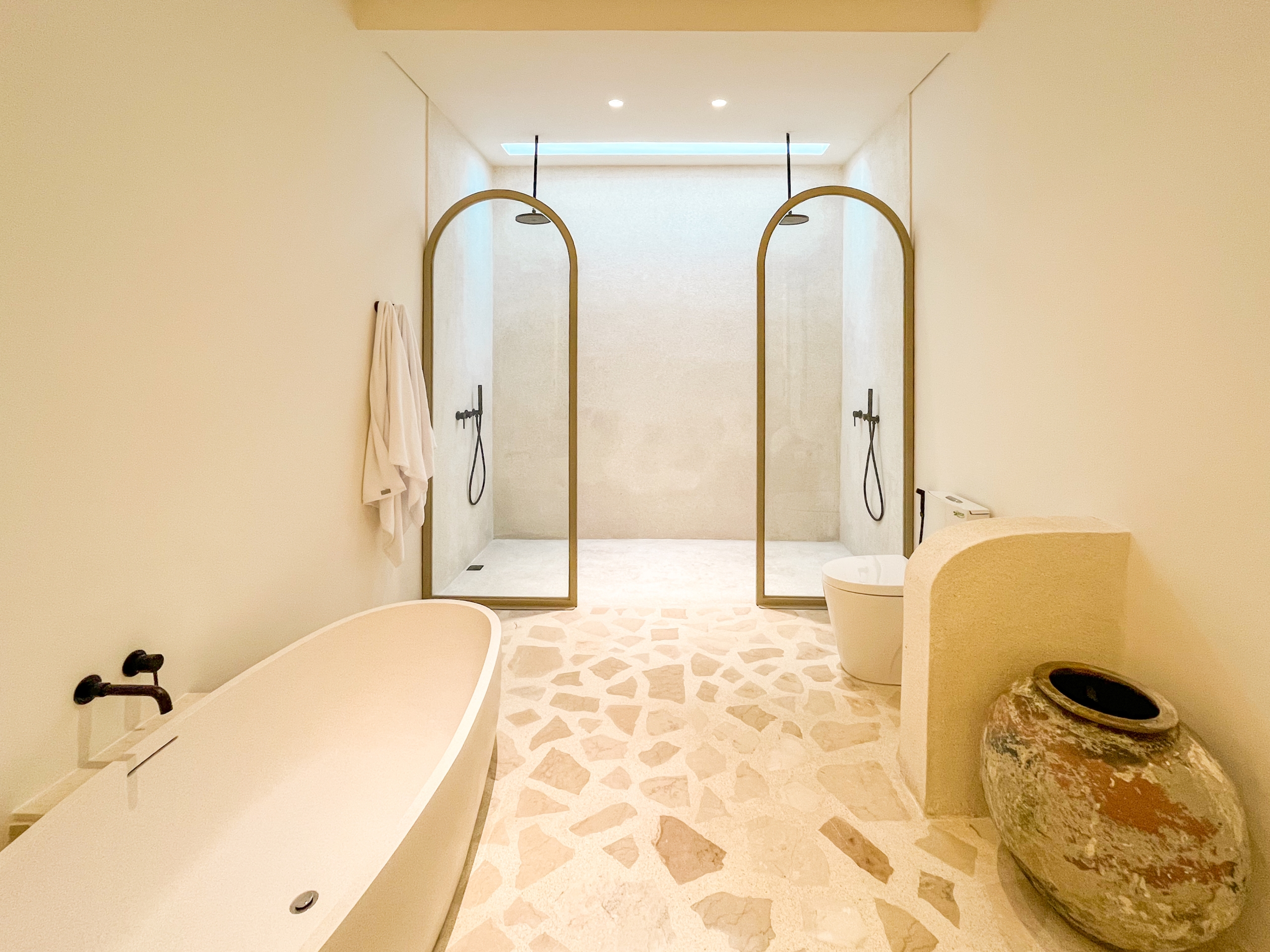 IMG_0502_4674-6a38c7b6742cf Spa-like bathroom with three arched-brass framed shower enclosures, a freestanding tub on the left, and terrazzo floors intact.