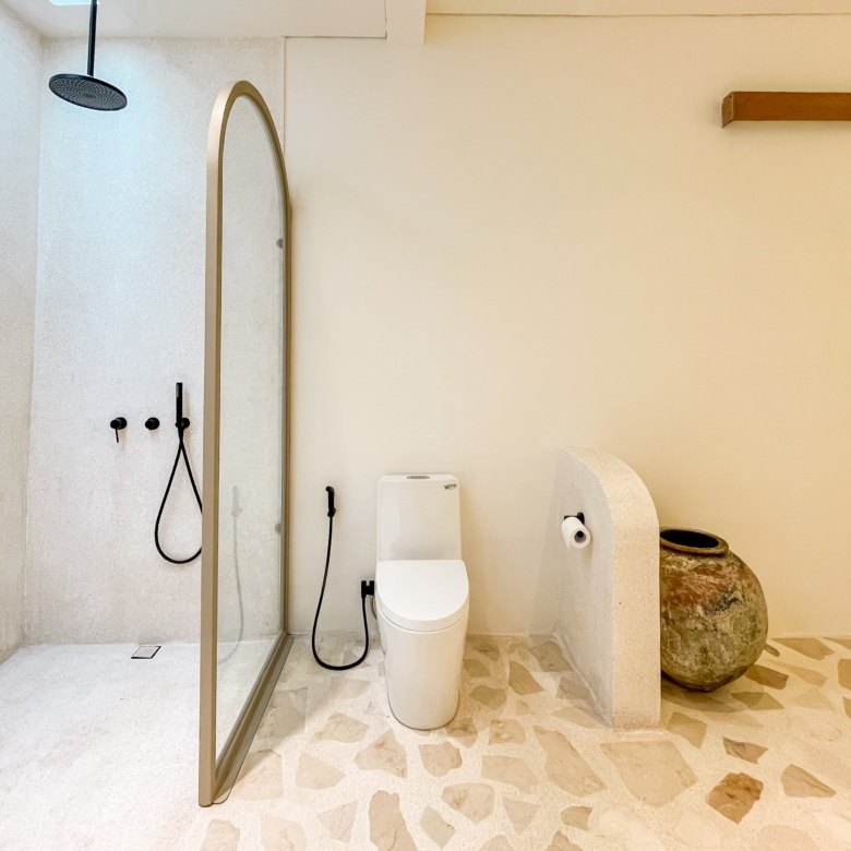 Modern bathroom with a glass-enclosed shower featuring a rainfall showerhead, a white toilet, and a tall mirror against beige walls.