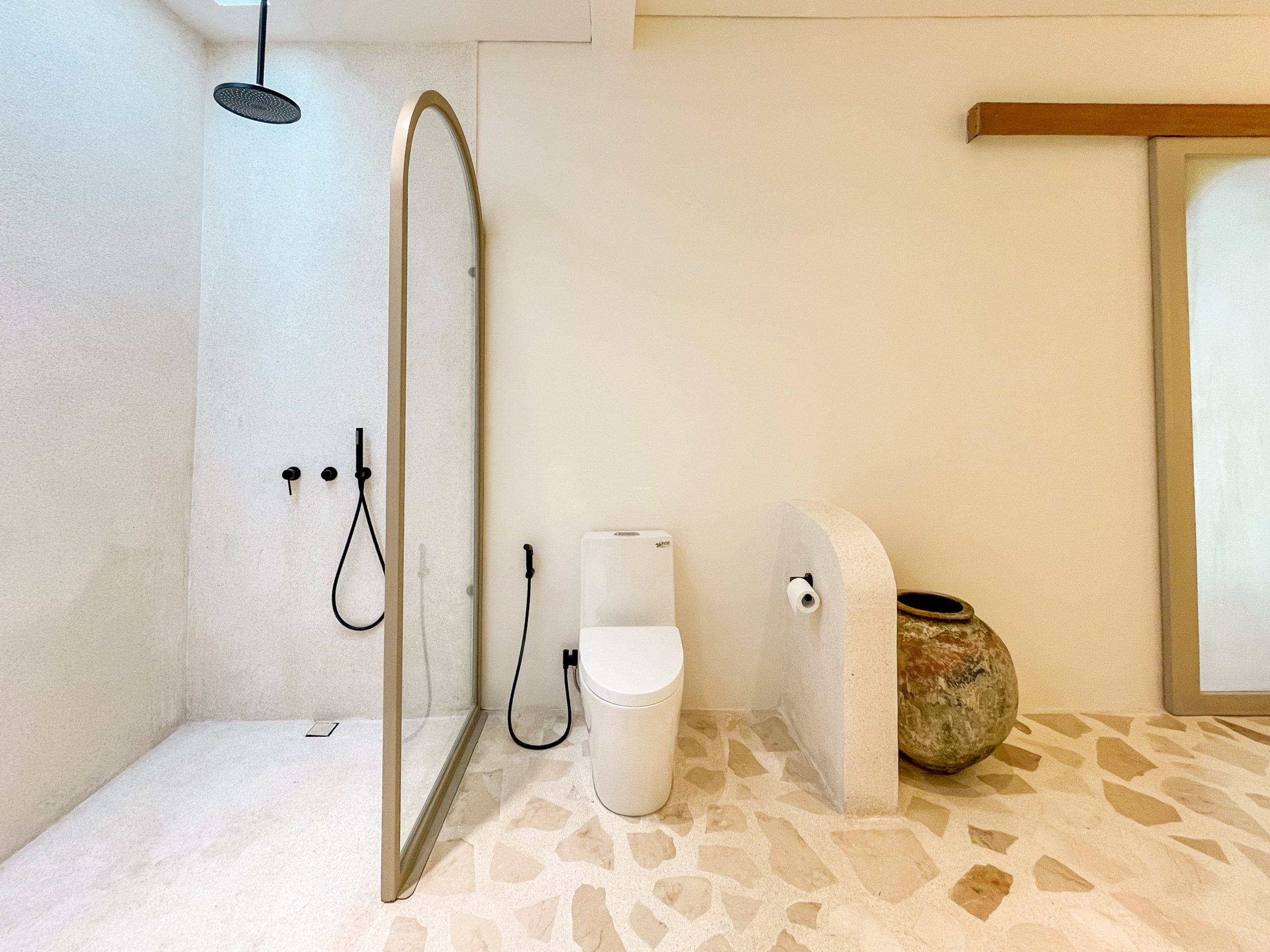 IMG_0514_4714-6a38c7b64a61d Modern bathroom with a glass-enclosed shower featuring a rainfall showerhead, a white toilet, and a tall mirror against beige walls.