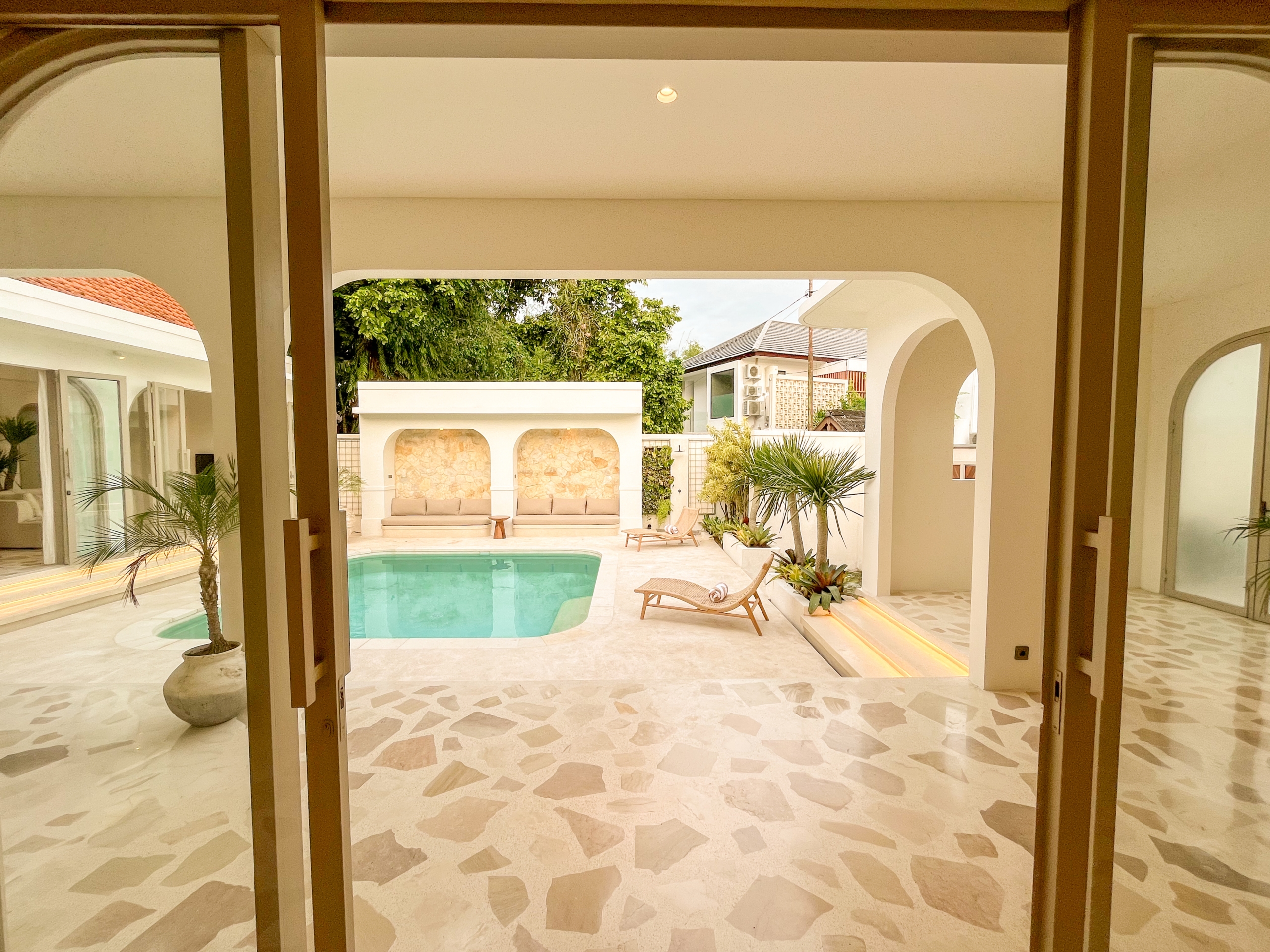IMG_0526_4681-6a38c7b45b4d9 Indoor villa courtyard with a turquoise pool, beige loungers, and greenery framed by white arches and doorways