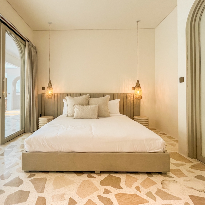 Hotel bedroom with a low platform bed, white linens, and woven pendant lights on either side.