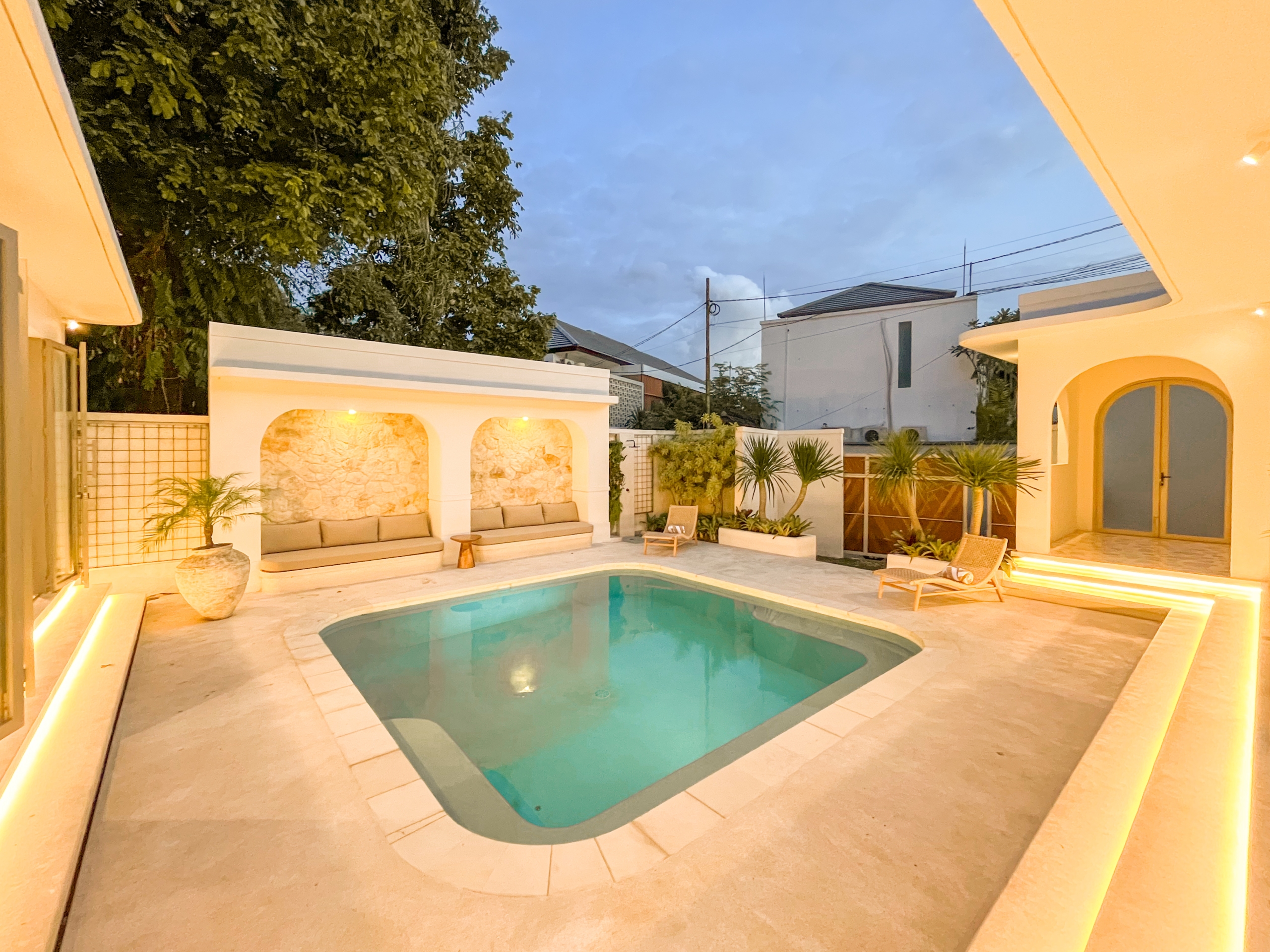 IMG_0600_4647-6a38c7b3e9da5 Backyard pool area with built‑in lounge seating, white arches, and warm lighting at dusk.
