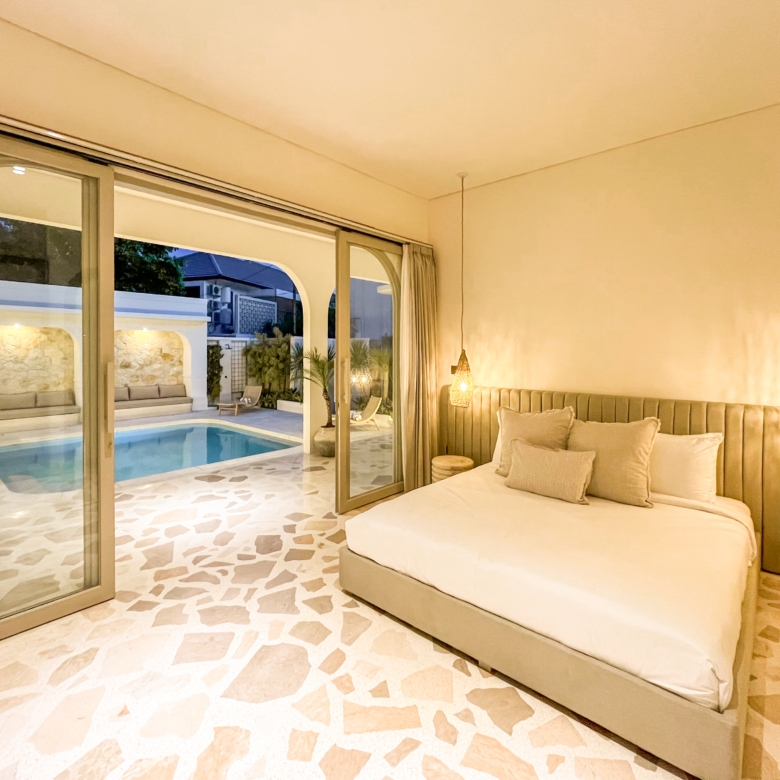 Hotel bedroom with a large beige bed, woven pendant lights, and sliding glass doors to an outdoor pool area.