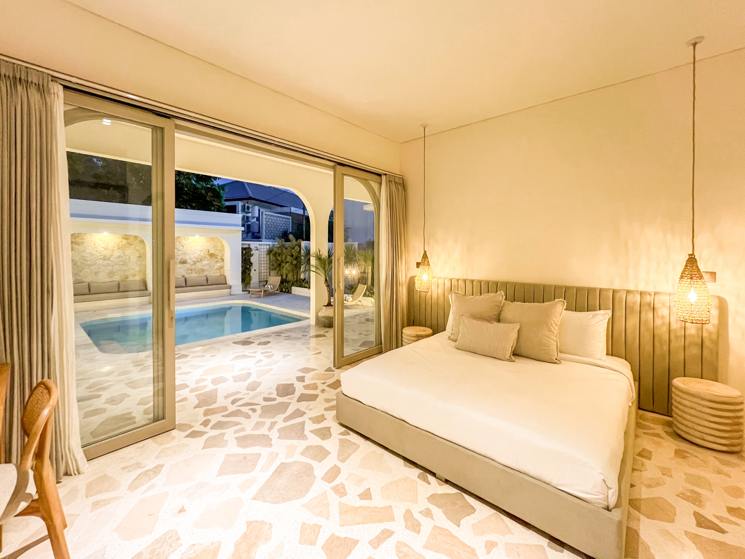 IMG_0612_4686-6a38c7b545fa2 Hotel bedroom with a large beige bed, woven pendant lights, and sliding glass doors to an outdoor pool area.