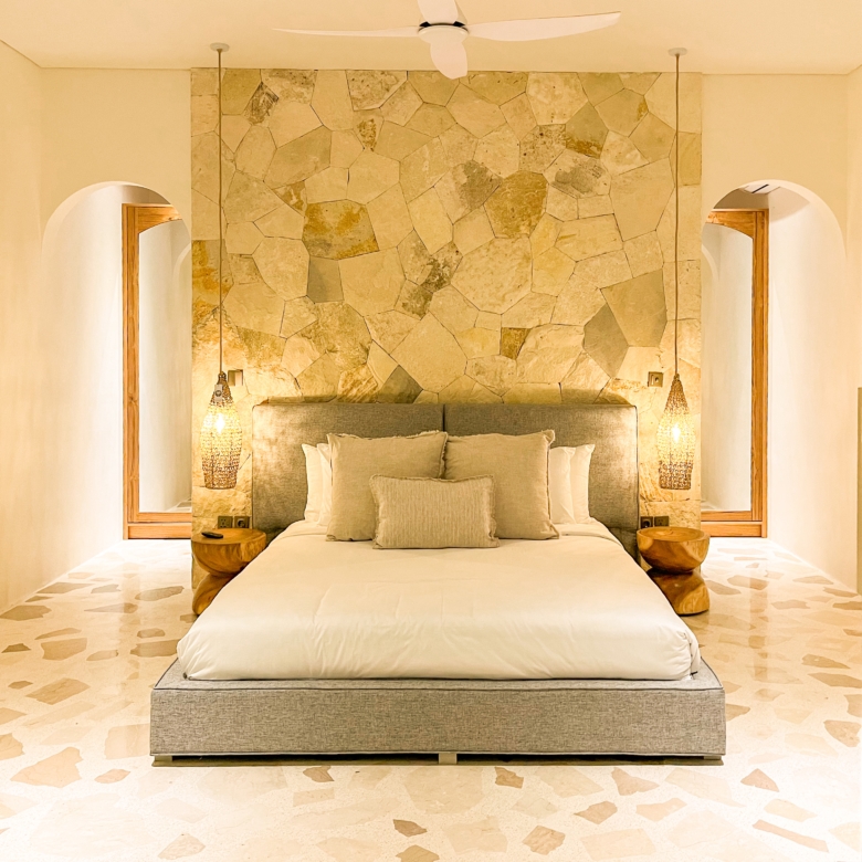 Hotel-style bedroom with a stone feature wall behind a low-profile bed and pendant lights on each side