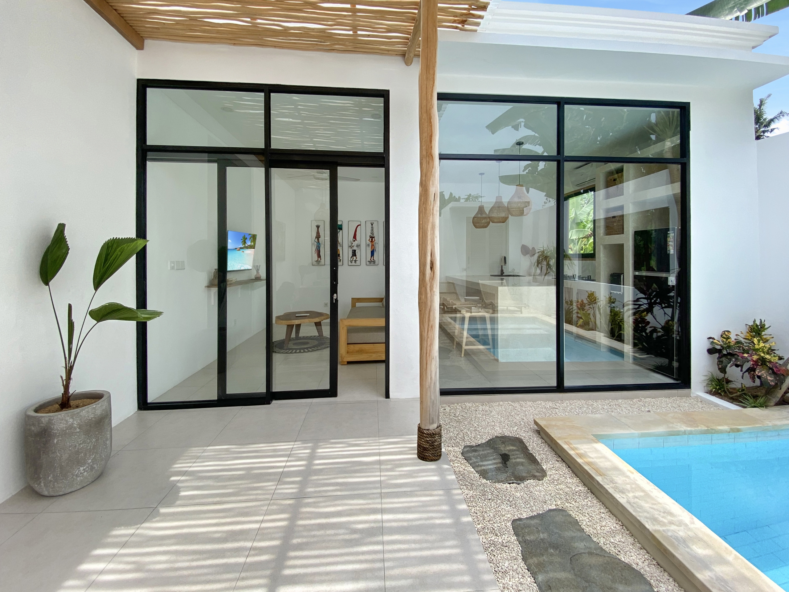 IMG_8105_5305-69ad009830ef2 Modern glass sliding doors with black frames opening to a bright interior, white walls, and a poolside view outside.