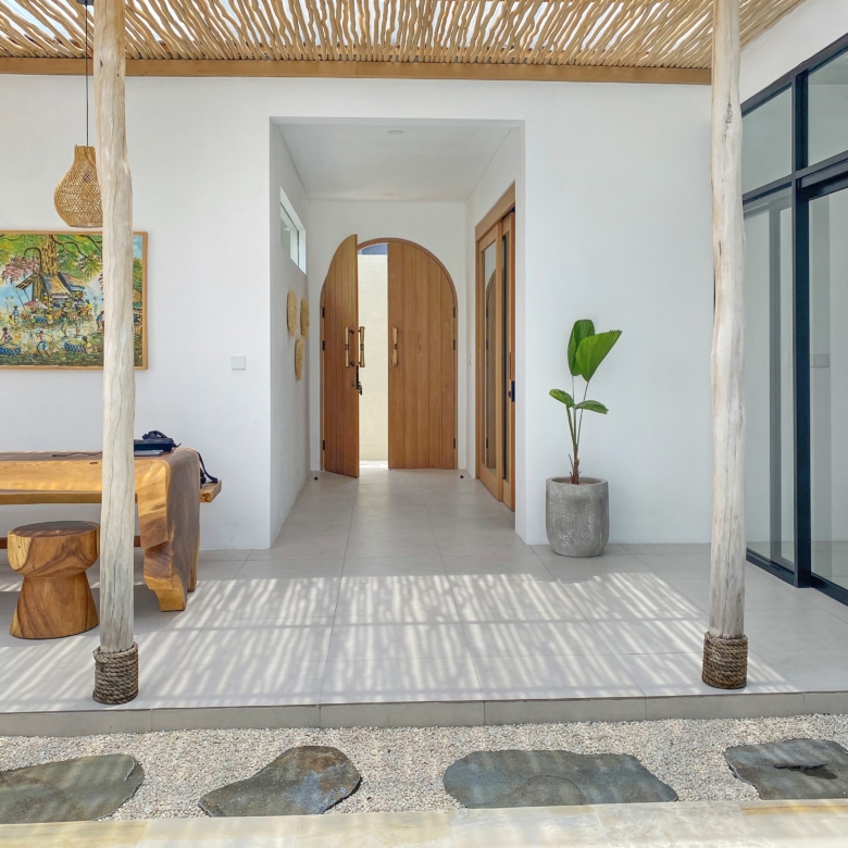 Interior hallway with arched wooden double doors, white walls, and a potted plant to the right near a glass wall edge.