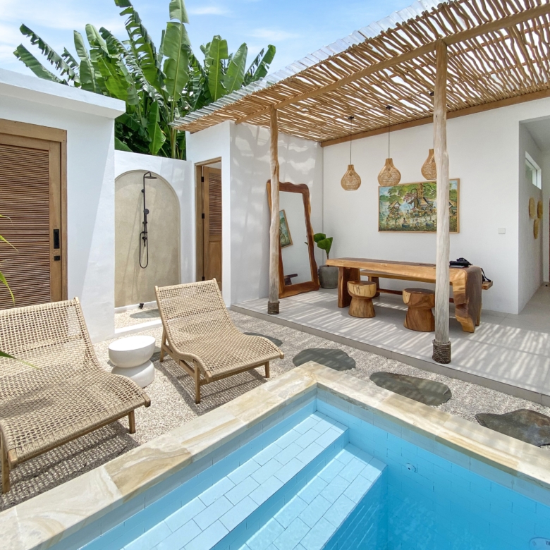Outdoor patio with a blue tiled pool, wicker lounge chairs, and a wooden pergola over a white-walled seating area.